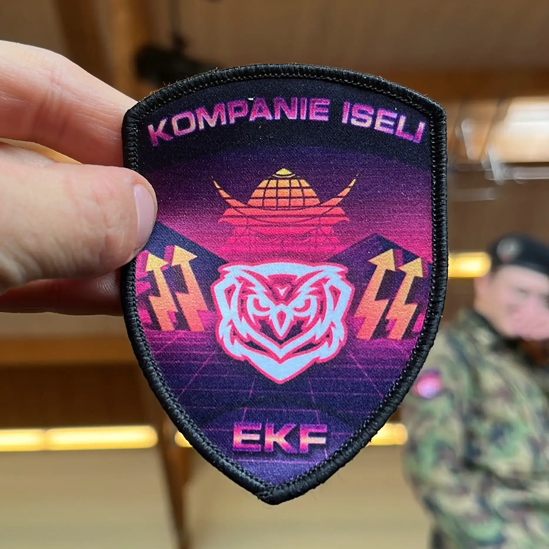 Militärisches Abzeichen von RS gekauft und hergestellt auf RS Badge. Man sieht eine Eule auf einem violetten vaporwave Hintergrund. Auf beiden Seiten sieht man eine Art Blitz, der aus dem weißen Boden kommt.
